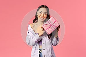 Curious whats inside. Portrait of cute silly asian girl shaking box with gift to guess what is it, smiling amused