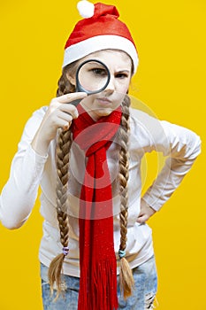 Curious Winsome Caucasian Teenager Girl in Santa Hat And Red Scarf Holding Empty Big Magnifying Glass While Searching and Posing