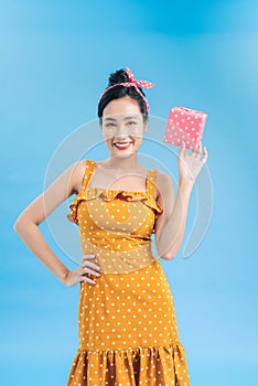 Curious woman in dress rejoicing her gift box. Young woman holding gift box with holiday present isolated on blue background