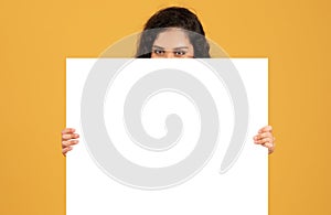 Curious woman peering over a blank white board with just her eyes and forehead showing