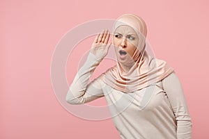 Curious young arabian muslim girl in hijab light clothes posing isolated on pink background in studio. People religious