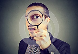 Curious young business man looking through a magnifying glass