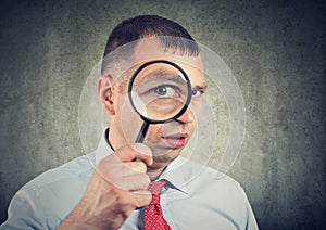 Curious young businessman looking through a magnifying glass