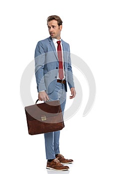 Curious young businessman with suitcase looking over shoulder