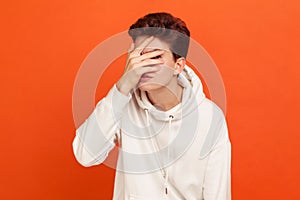 Curious young man in casual sweatshirt with hood looking through fingers, scared teenager looking with apprehension, spying