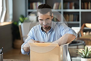 Curious young man in eyeglasses unpacking huge cardboard box.