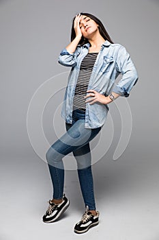 Curious young woman covering face with hand and looking at camera while standing against grey background
