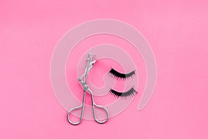 Curled and thick eyelashes. False eyelashes and eyelash curler on pink background top view copy space