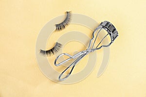 Curler and false eyelashes on color background