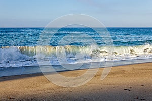 Curling breaking wave tube, foaming with backwash on sandy shore