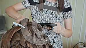 Curling hair in beauty salon. Professional hairdresser using curling iron for hair curls at salon.