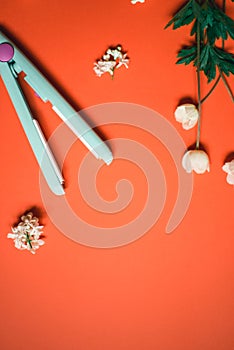 Curling iron ripple on a coral background. Hair accessory on orange background with flowers. Hairstyle tool