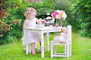 Curly adorable toddler girl playing tea party with doll