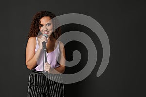 Curly African-American woman in stylish clothes posing with microphone on black background.