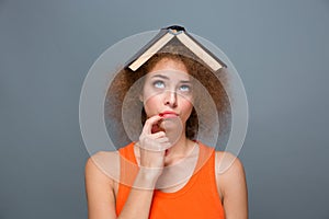 Curly annoyed woman looking funny with book on head