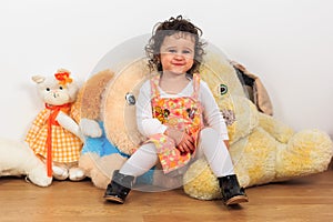 Curly baby girl smiling and sitting on a plush dog toy