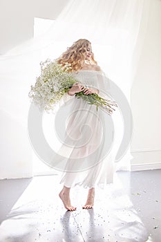 Curly blonde romantic look, beautiful eyes. White wildflowers in hands. Girl white light dress and curly hair, portrait of woman