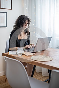Curly brunette freelancer woman working remotely use laptop at cozy home scandinavian interior