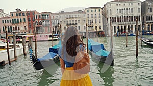 Curly brunette girl stands, looks postcard view gondolas, Grand Canal. Rear view