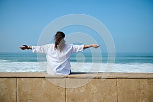 Curly brunette outstretches her arms to the sides, enjoying mesmerizing view of beautiful waves pounding on the shore.