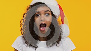 Curly brunette in Santa hat saying Wow, surprised with Xmas gift, festive mood