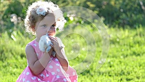 A curly child holds a beautiful white bunny in her hands. A pet rabbit