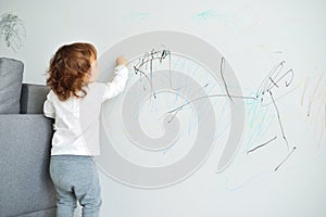 Curly cute little baby girl drawing with crayon color on the wall. Works of child