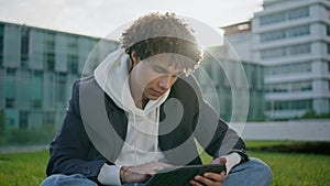 Curly freelancer working tablet at grass closeup. Calm blogger sitting lawn