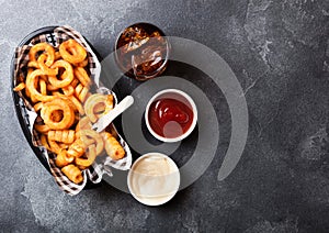 Curly fries fast food snack in red plastic tray with glass of cola and ketchup on stone kitchen background. Unhealthy junk food