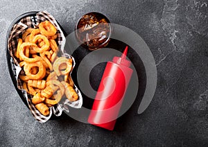 Curly fries fast food snack in red plastic tray with glass of cola and ketchup on stone kitchen background. Unhealthy junk food