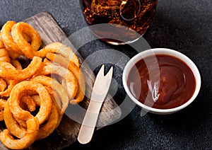 Curly fries fast food snack on wooden board with ketchup and glass of cola on stone kitchen background. Unhealthy junk food