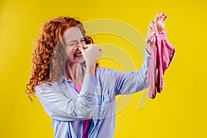 Curly ginger redhead woman in a cotton shirt gesture smells bad holding a dirty pink sock out a disgusted look on her