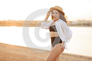 Curly girl in a black swimsuit by the sea in a hat