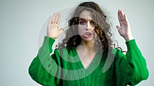 Curly girl in a green sweater with braces closes her face with her hands and shows various emotions. Parisian girl in