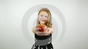 A curly girl holds out an apple to the camera. A beautiful child offering a large red apple