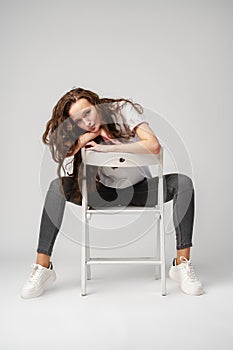 Curly girl model posing on a chair against gray background