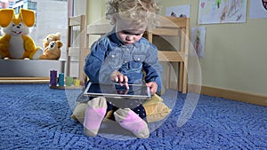 Curly girl play tablet sit on blue carpet. Modern media technology. 4K