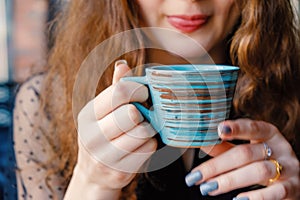 A curly girl with red hair poses in a cafe holding a Japanese-style cup at her juicy lips