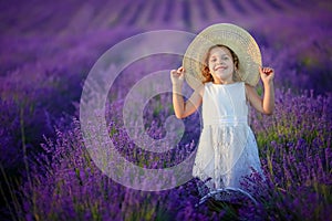 Curly girl standing on a lavender field in white dress and hat with cute face and nice hair with lavender bouquet and