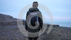 Curly guy with backpack lonely walks a desert coast in late autumn