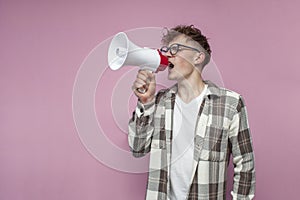 Curly guy with glasses shouts loudly into a megaphone an announcement on a pink background