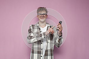 Curly guy with glasses uses a smartphone and smiles on a pink background, a man presses his finger on the touch screen