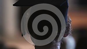 Curly guy in mortarboard watching happy graduation ceremony, university