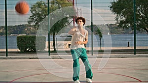 Curly guy playing basketball on sports field. Skilful teenager throwing ball