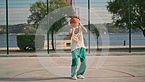 Curly guy playing basketball on sports field. Skilful teenager throwing ball