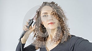 Curly hair. Beautiful brunette woman with curly hair, curls her hair, uses curling tongs to get fine curls. Hairstyles