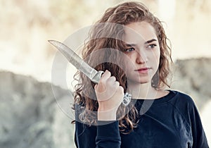 Curly hair. Beautiful girl with wavy hair with big knife, a blade near the face, threatens