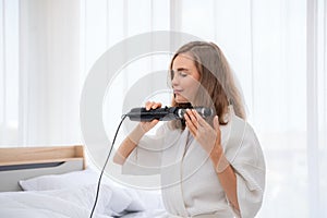 Curly Hair. Beautiful Smiling Woman With Long Blonde Wavy Hair Ironing It, Using Curling Iron. Happy Girl With Gorgeous Healthy