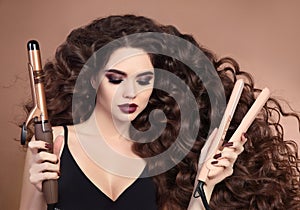 Curly hair. Beauty Close-up of brunette girl with blowing hairstyle holding curling and straightening iron. Marsala eye shadow ma