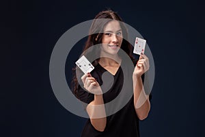 Curly hair brunette is posing with playing cards in her hands. Poker concept on a black background. Casino.